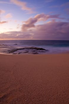 Waves froth along the ocean shore during sunset in oahu hawaii.