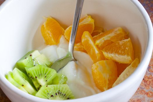 Kiwis and oranges are topping plain yogurt in a white bowl showing an example of a healthy breakfast meal.