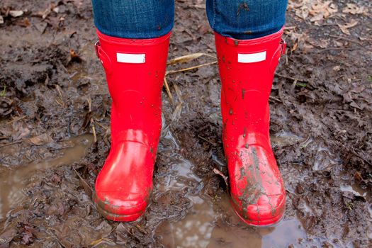 Red rain boots on the legs of a girl after she played in the mud and got them dirty and muddy.