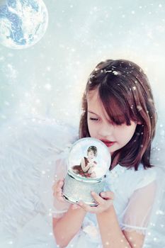 Little angel holds a snow globe and watches a little girl inside blowing snow.