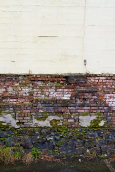 An old decayed brick wall has plants growing on it and pieces of the bricks turning to rubble