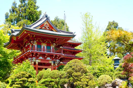 A bright red Japanese pagoda building in a tea garden sits peacefully.