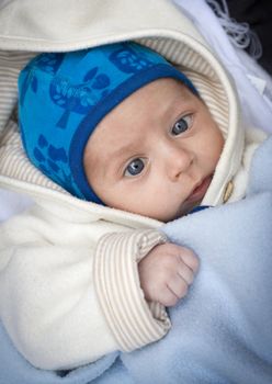 A new born baby with a blue hood cuddled up in a blanket