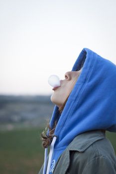 A young teenage girl in hoodie blowing a chewinggum bubble