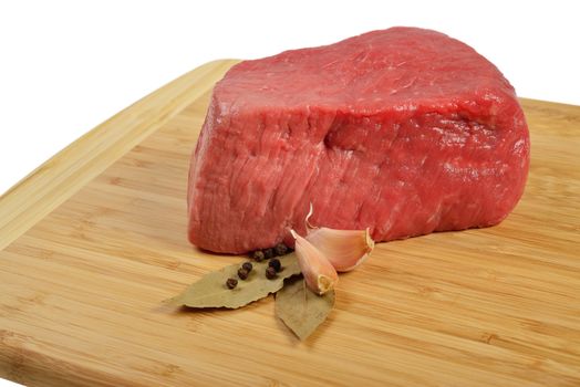 Piece of raw beef on a wooden board, decorated with garlic and bay leaves.