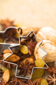 Christmas tree cookie cutter on baking ingredients (walnut, cinnamon, anise, raisin,sultana and almond) (Selective Focus, Focus on the cookie cutter) 