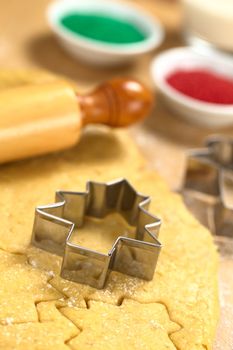 Baking Christmas Cookies: Cookie cutter on rolled out sugar or butter cookie dough with rolling pin and colorful sprinkles in the back (Selective Focus, Focus on the lower edge of the cookie cutter) 