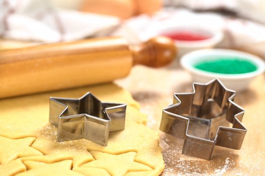 Baking Christmas Cookies: Cookie cutter on rolled out sugar or butter cookie dough with rolling pin and colorful sprinkles in the back (Selective Focus, Focus on the lower edges of the star- and tree-shaped cookie cutters) 