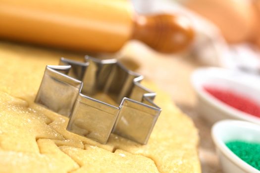 Baking Christmas Cookies: Cookie cutter on rolled out sugar or butter cookie dough with rolling pin in the back and colorful sprinkles on the side (Selective Focus, Focus on the lower edge of the cookie cutter) 