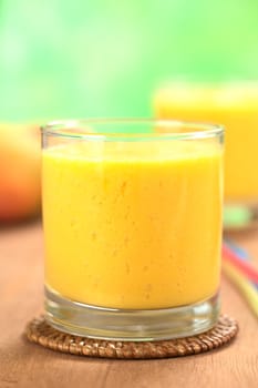 Fresh homemade mango juice in glass with another juice and mango fruits in the back (Selective Focus, Focus on the front upper part of the drink)