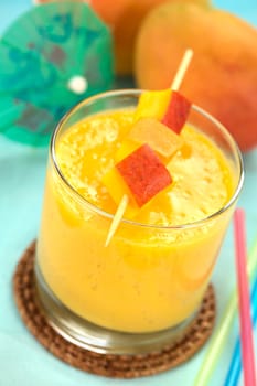 Fresh homemade mango juice in glass with mango pieces on skewer on the top of the drink (Selective Focus, Focus on the first mango piece)