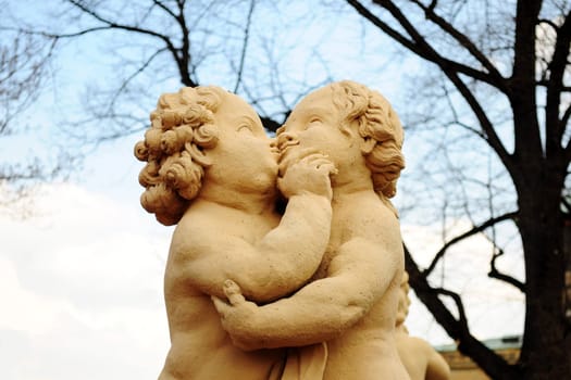 The ancient statue of two children with the sky and bare trees on the background, in a city park of Dresden, Germany