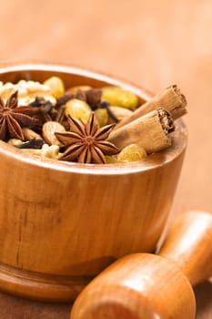 Baking ingredients such as star anise, clove, cinnamon, almond, raisin, sultana and walnut in wooden mortar with pestle in front (Selective Focus, Focus on the middle of the star anise in the front) 