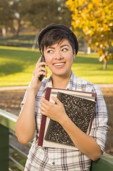 Outdoor Portrait of a Pretty Mixed Race Female Student Holding Books and Talking on Her Cell Phone on a Sunny Afternoon.