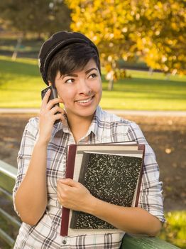 Outdoor Portrait of a Pretty Mixed Race Female Student Holding Books and Talking on Her Cell Phone on a Sunny Afternoon.