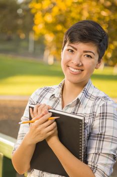 Outdoor Portrait of a Pretty Mixed Race Female Student Holding Books on a Sunny Afternoon.