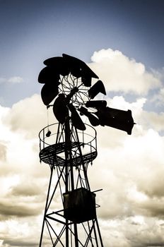 Old Farm Windmill for Pumping Water with Spinning Blades against cloudy sky.