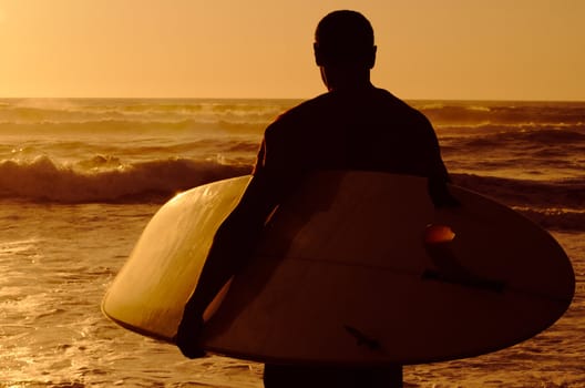 A surfer watching the waves at sunset in Portugal.