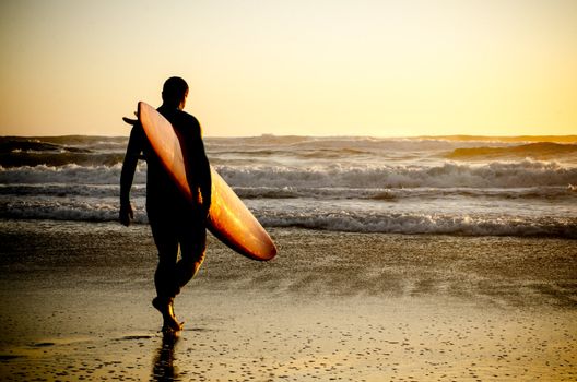Surfer walking on the beach with the waves at sunset in Portugal.