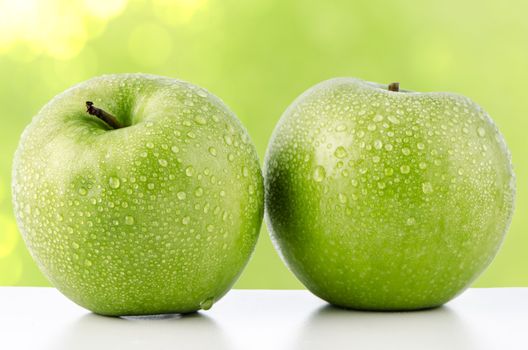 Two fresh green apples on green defocused background.