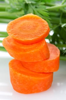 Pile of carrot slices and green parsley leaves closeup on white reflective background.