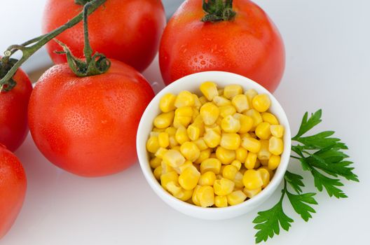 Corn grains on bowl and cherry tomatoes vine on white background.