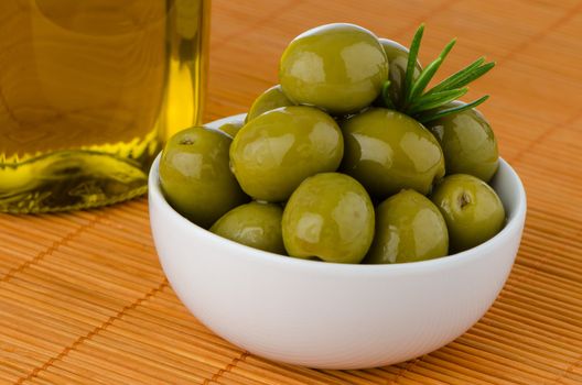 Green olives in a white ceramic bowl on orange  background.