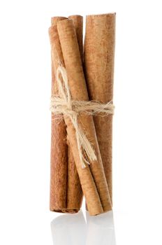 Cinnamon sticks, tied by rope on white reflective background.