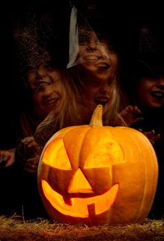 Portrait of little girl in black hat and black clothing with pumpkin on black background