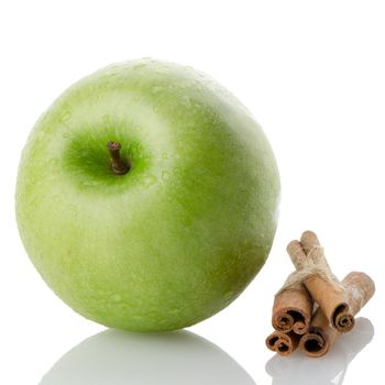 Ripe green apple with cinnamon sticks over reflective white background