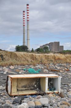 Trashed fridge on the seashore next to a factory