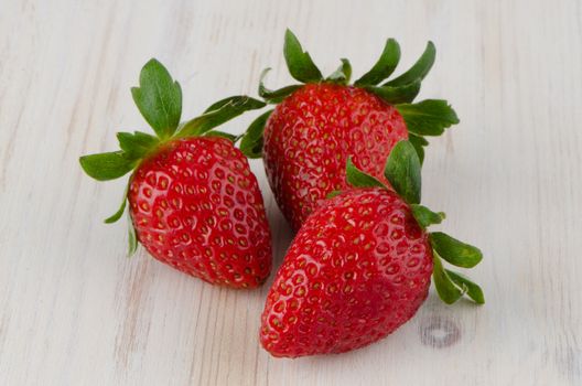 Three fresh strawberries on white  wooden background.