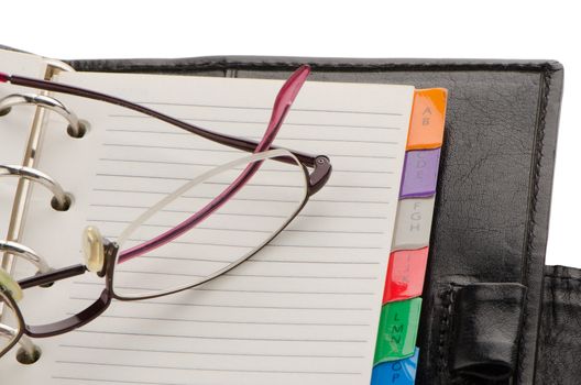 Leather notebook and glasses on white reflective background.