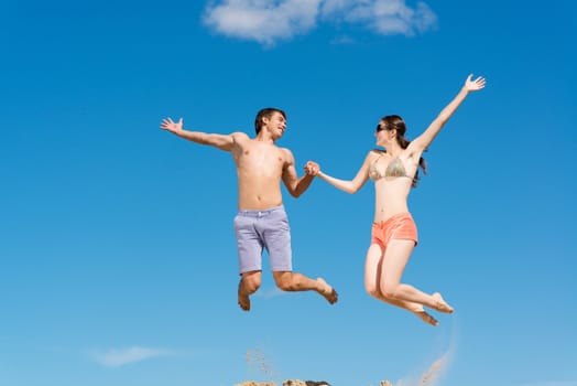 couple jumping together holding hands on a background of blue sky