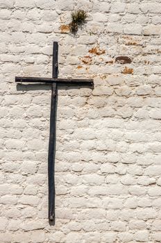 A rustic wooden cross on a white brick wall