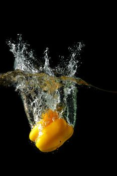 Colored yellow paprika in water splashes on black background