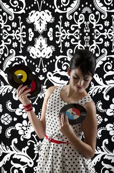 young woman in front of a black and white textured background with 60's inspired style, holding three small record choosing one to play