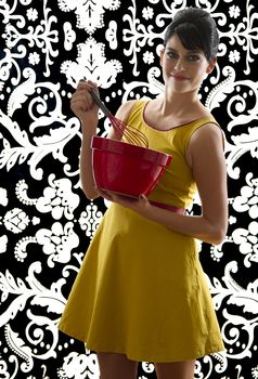 young woman in front of a black and white textured background with 60's inspired style, holding a red whisk in a red bowl