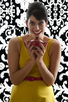 young woman in front of a black and white textured background with 60's inspired style, holding a red miniature crockpot