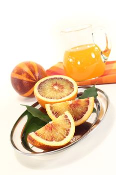 two fresh red-yellow blood orange with leaves and juice on a bright background