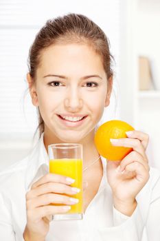 Young smiling woman holding glass of juice and orange at home