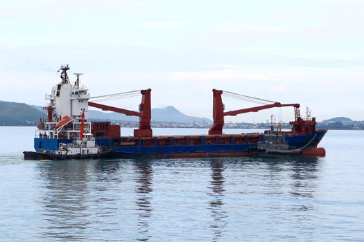 Tugboat assisting bulk cargo ship to harbor quayside