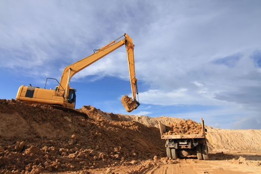 Heavy excavator loading dumper truck with sand in quarry over blue sky