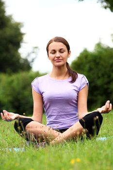 Young and beautiful woman doing her yoga workout on the park`s lawn