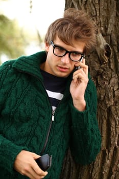 Closeup of young and handsome guy with cellphone in the autumn park