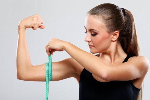Beautiful fitness girl measure her biceps with a ruler over grey background