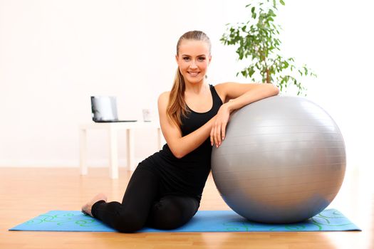 Happy and beautiful woman with fitness ball on blue mat at home