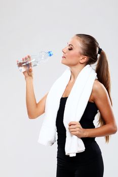 Beutiful fitness woman drink water on grey background