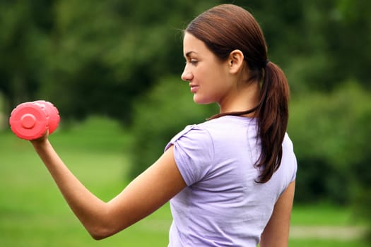 Young woman doing her fitness exercises with red dumbbells in the park