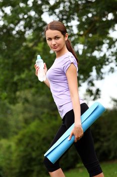Portrait of young and beautiful girl with fitness mat in the park